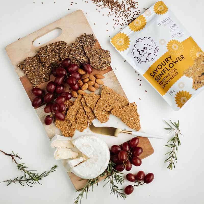 A cheese platter from Eve’s Crackers filled with Savoury Sunflower crackers, red grapes, almonds and a round of Brie cheese.