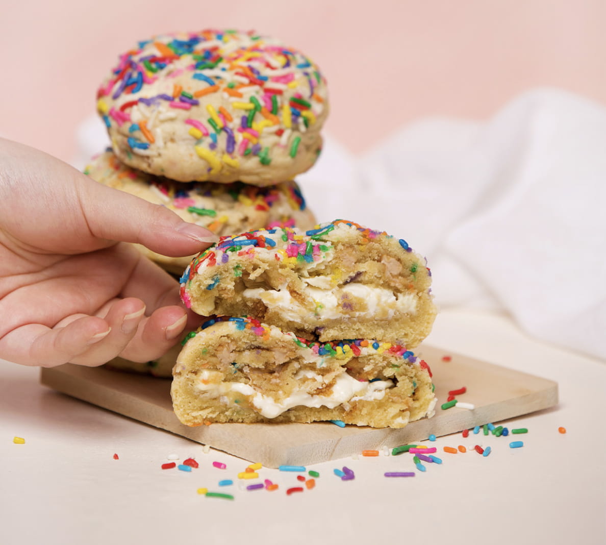 A woman reaches for a half of a YVR stuffed cookie that’s coated with rainbow sprinkles.