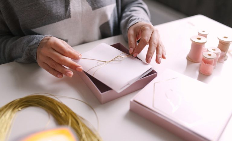 A woman ties a bow around a wedding invitation at a crafts table.